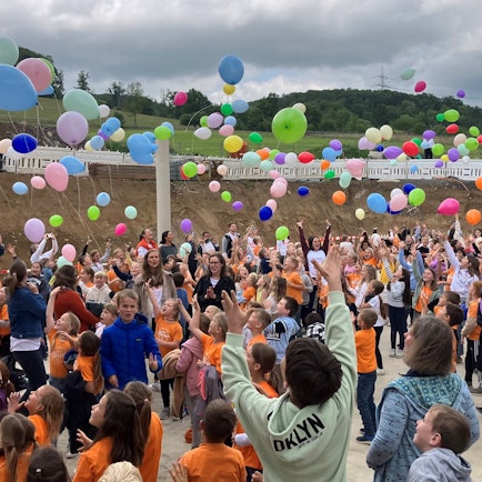 Schülerinnen und Schüler sowie Lehrkräfte lassen bunte Luftballons steigen.