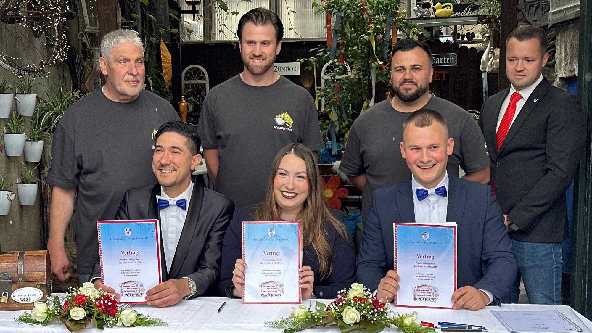 Das künftige Porzer Dreigestirn 2026 mit seinen Adjutanten hält die frisch unterschriebenen Verträge hoch: Prinz Maik I., Jungfrau Jil und Bauer Joel (v.r.).
