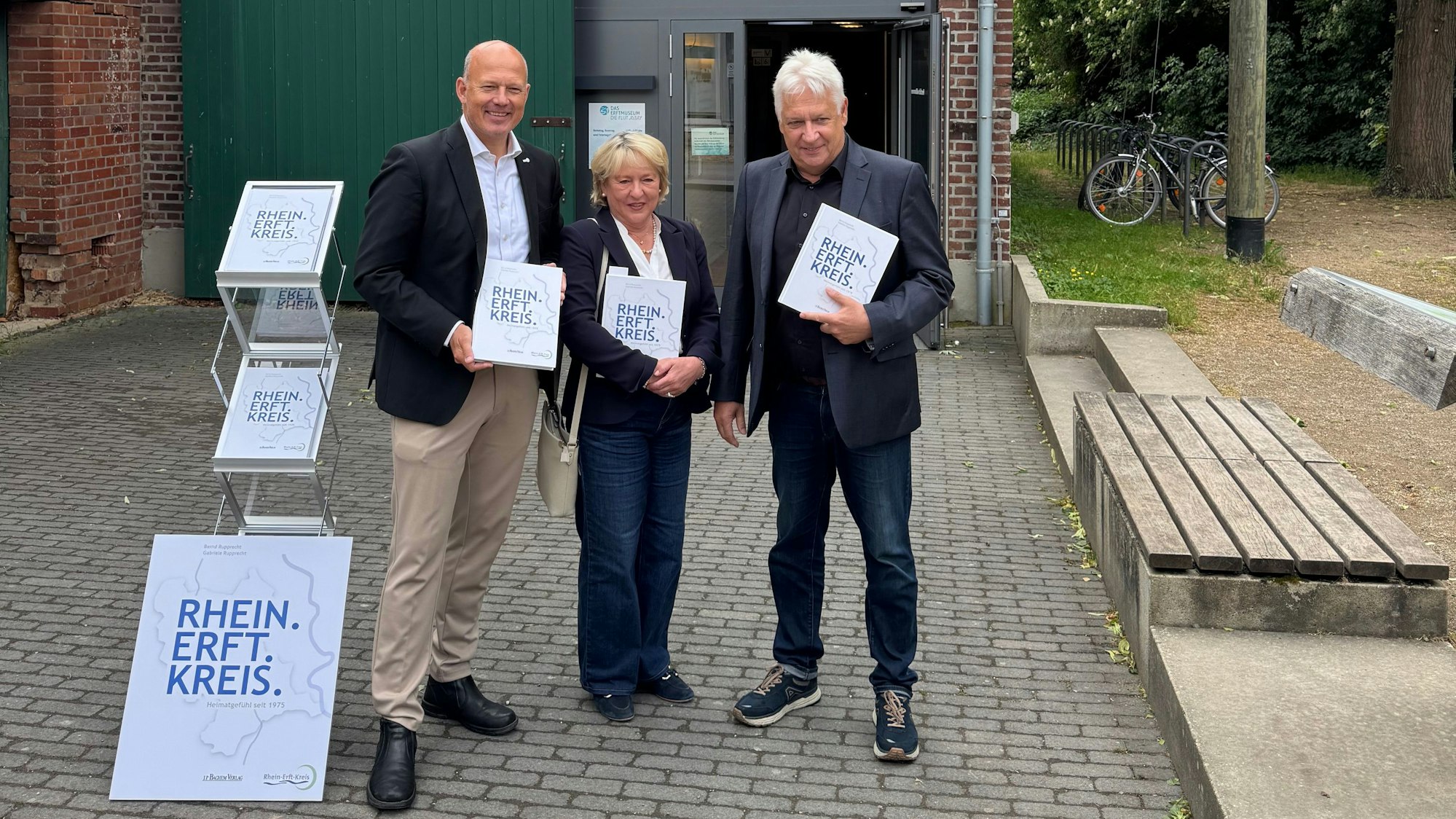 Eine Frau und zwei Männer halten jeweils ein Buch.