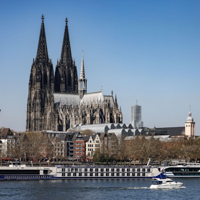 Ein Boot fährt bei sonnigem Wetter am Kölner Dom vorbei über den Rhein.