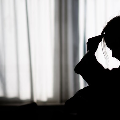 Die Silhouette einer Frau zeichnet sich vor einer hellen Fensterfront ab.