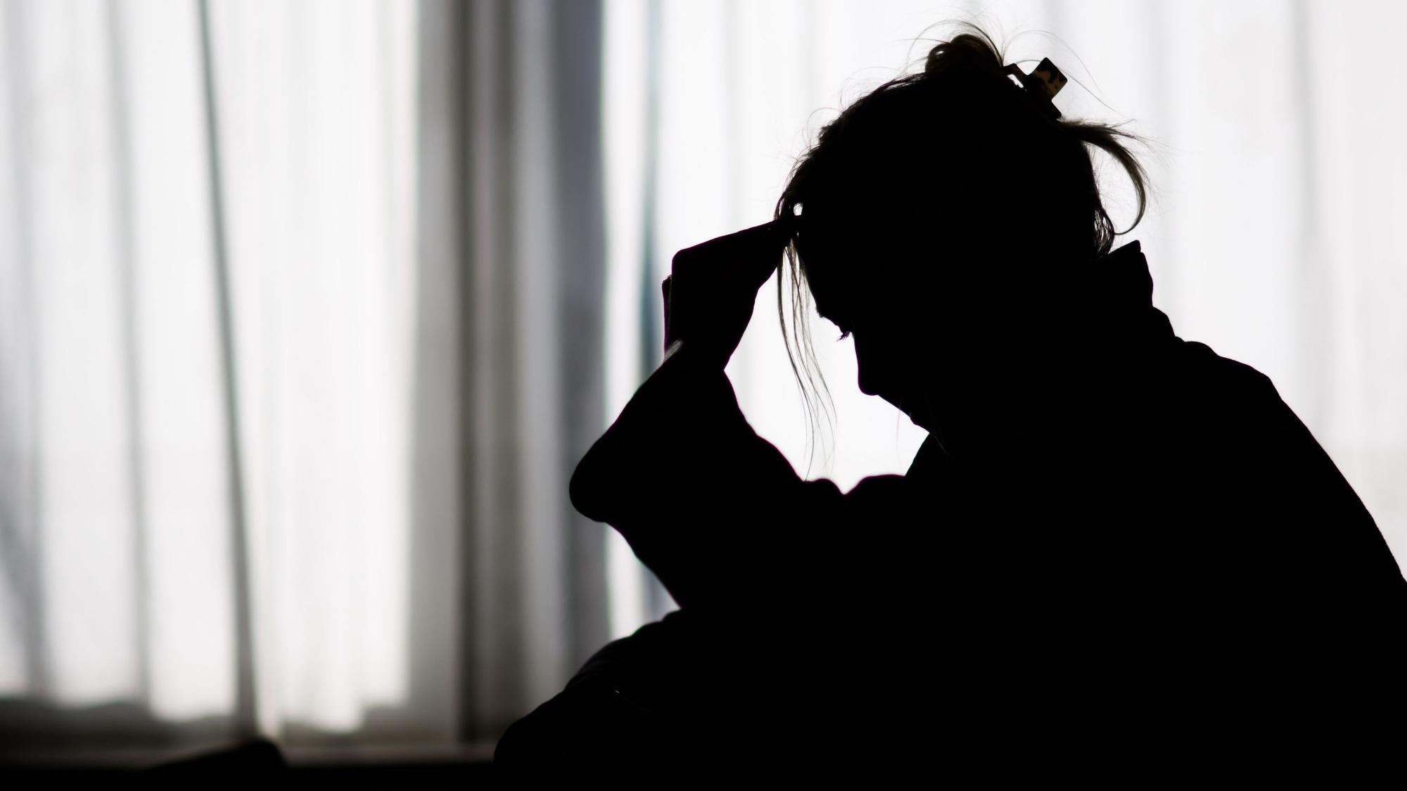 Die Silhouette einer Frau zeichnet sich vor einer hellen Fensterfront ab.