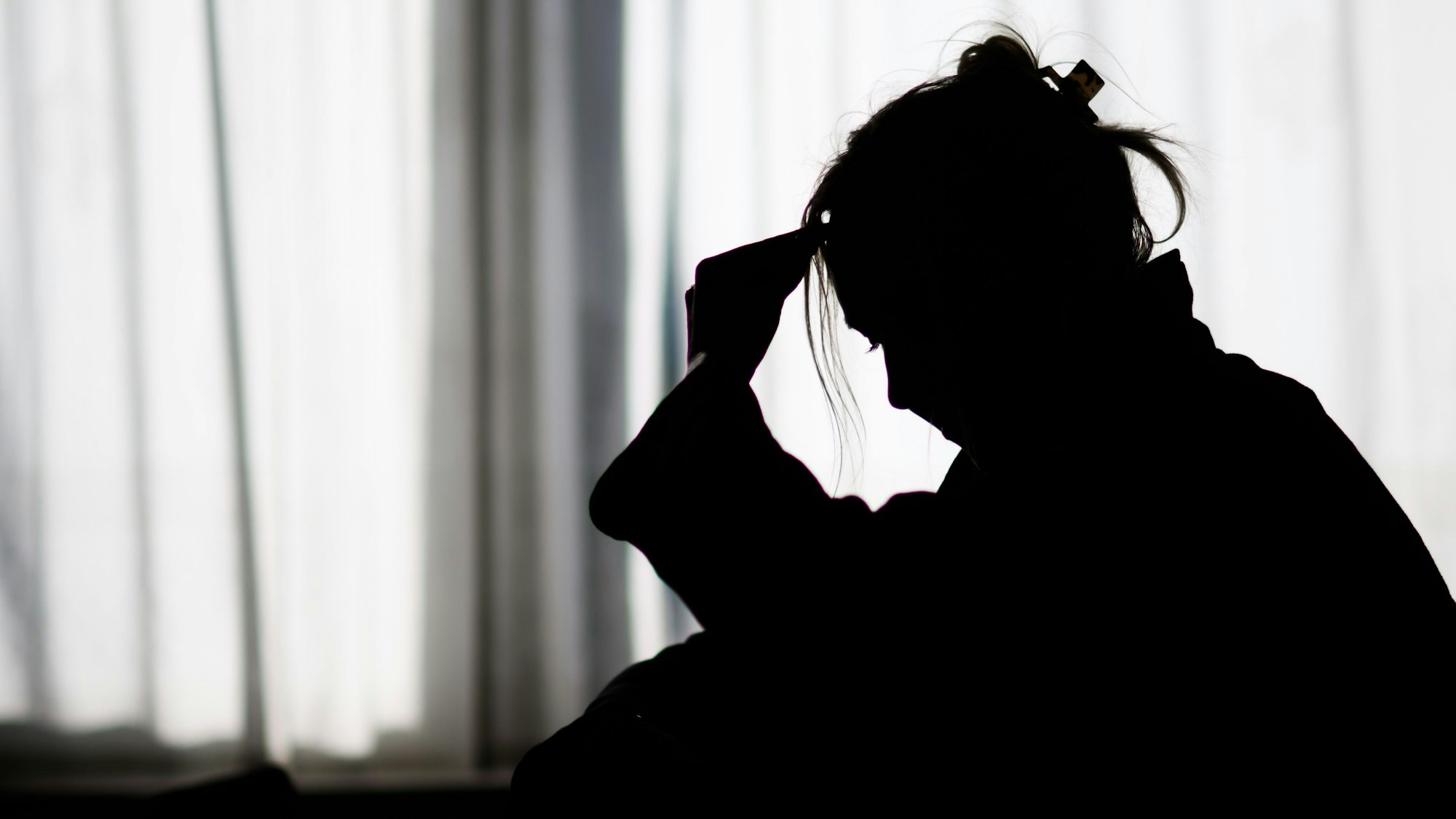 Die Silhouette einer Frau zeichnet sich vor einer hellen Fensterfront ab.