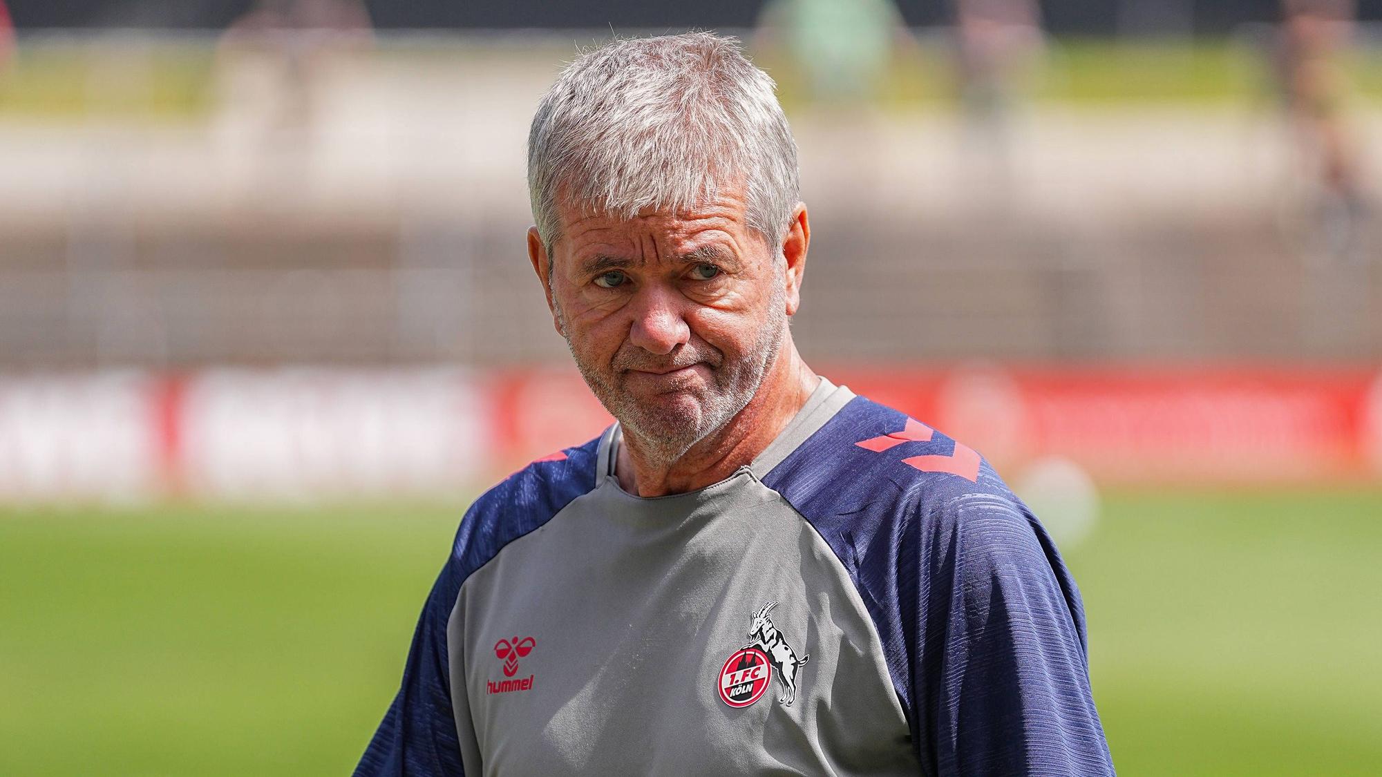FC-Trainer Friedhelm Funkel schaut frustriert. Im Hintergrund sind unscharf Rasen und Tribünen eines FC-Trainingsplatzes zu sehen.