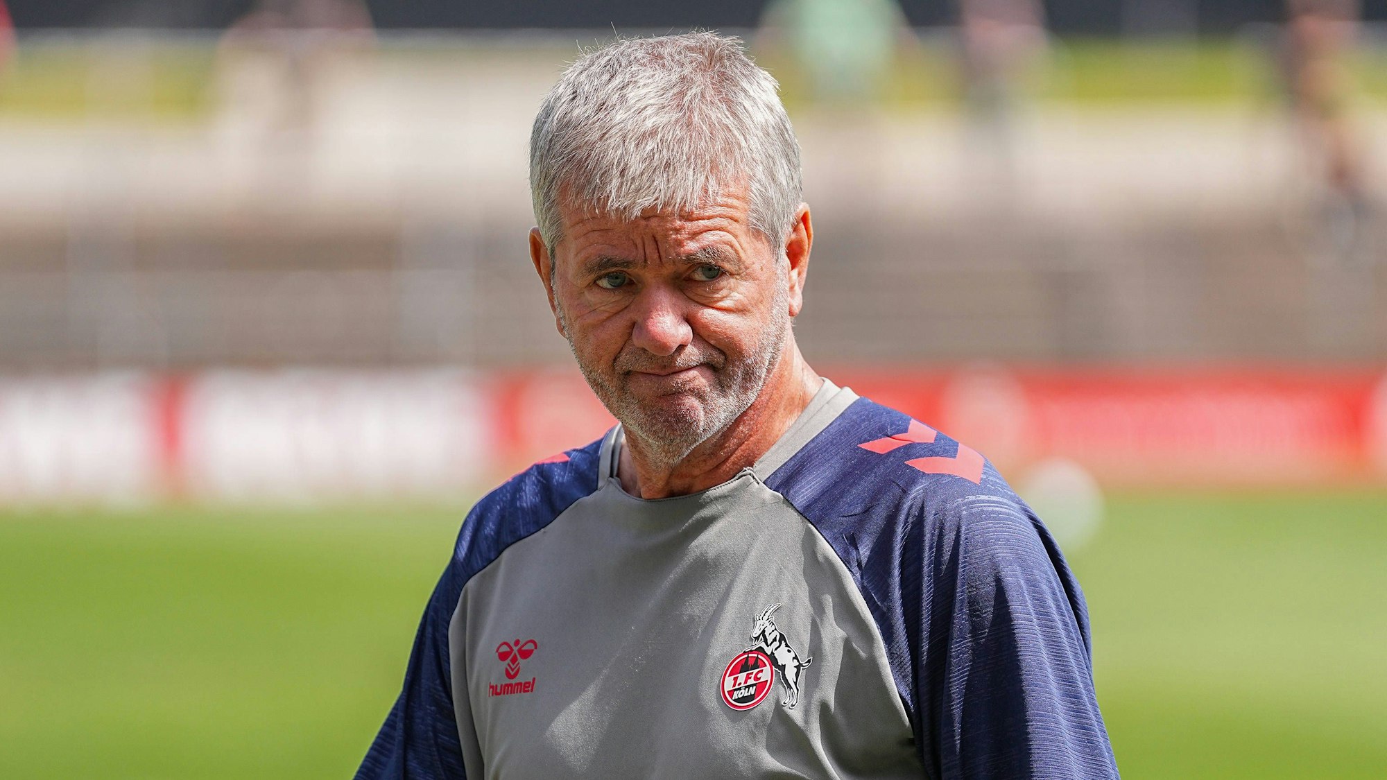 FC-Trainer Friedhelm Funkel schaut frustriert. Im Hintergrund sind unscharf Rasen und Tribünen eines FC-Trainingsplatzes zu sehen.
