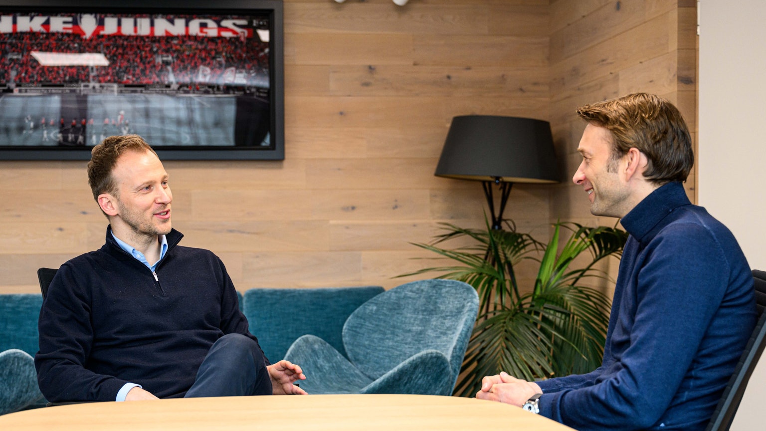Zwei ehemalige Fußballprofis sitzen an einem Tisch zusammen und besprechen sich.