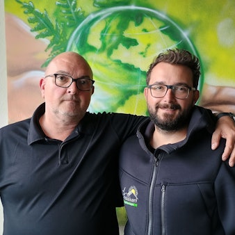 Oliver Dinslaken hat den Arm um seinen Sohn Max gelegt. Hinter ihnen ist ein Graffito, das einen grünen Globus und die Kölner Hohenzollernbrücke zeigt.