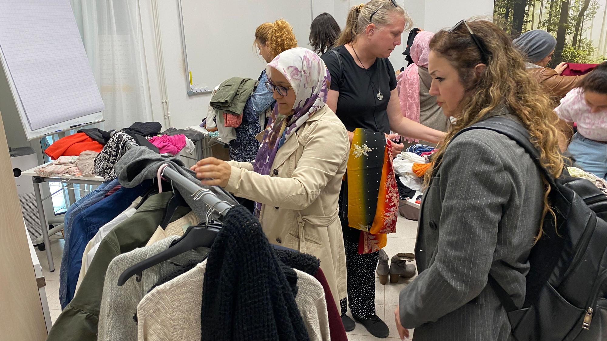 Mehrere Frauen sehen sich Kleidung an, die auf Tischen liegt oder an Ständern hängt.