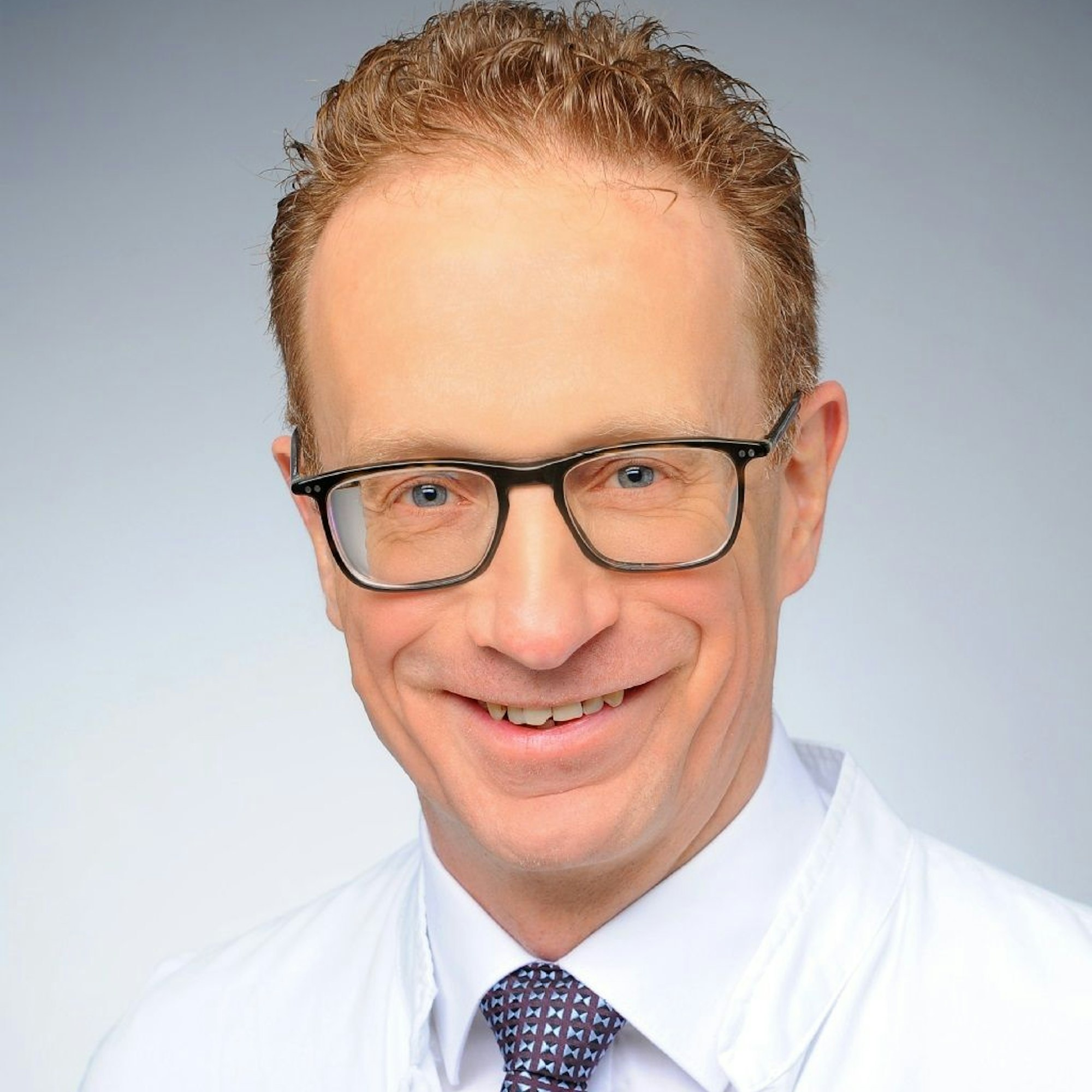 Herr Heidenreich ist im Porträt zu sehen, er trägt Brille, hat kurzes rotes Haar und lächelt in die Kamera.