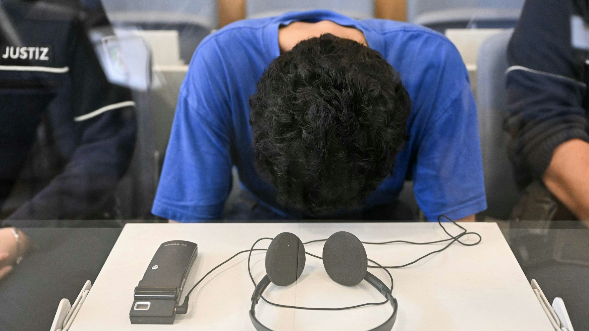 Der Angeklagte hat seinen Kopf fast bis zum Tisch gesenkt.