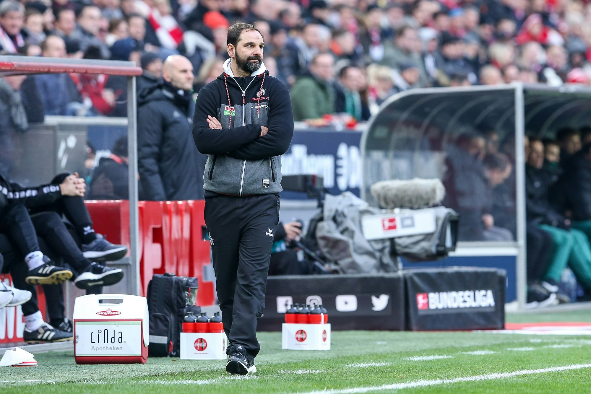 Ein Fußballtrainer steht mit verschränkten Armen am Seitenrand.