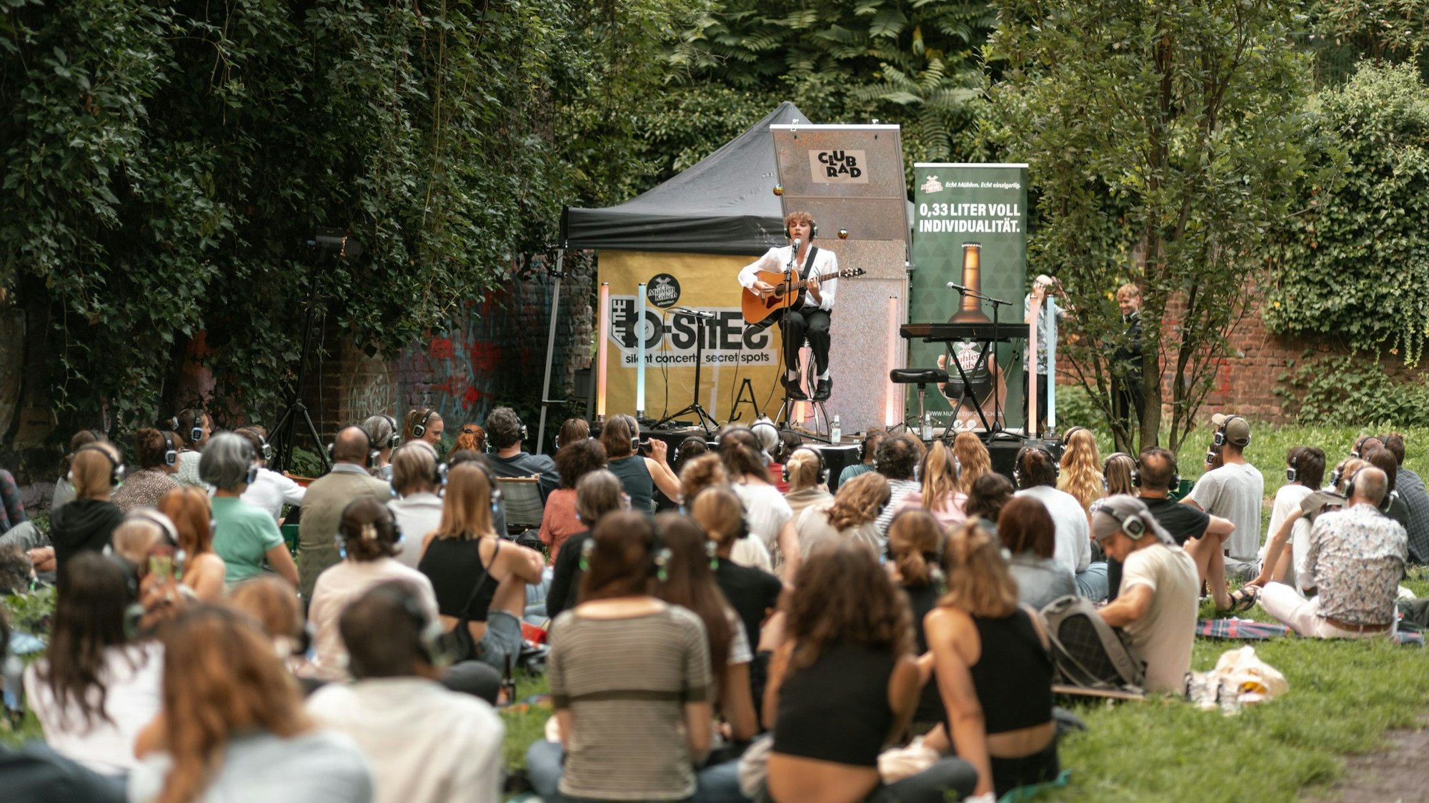 Gäste in einem Park mit Kopfhörer, auf der Bühne der Sänger Oskar Haag