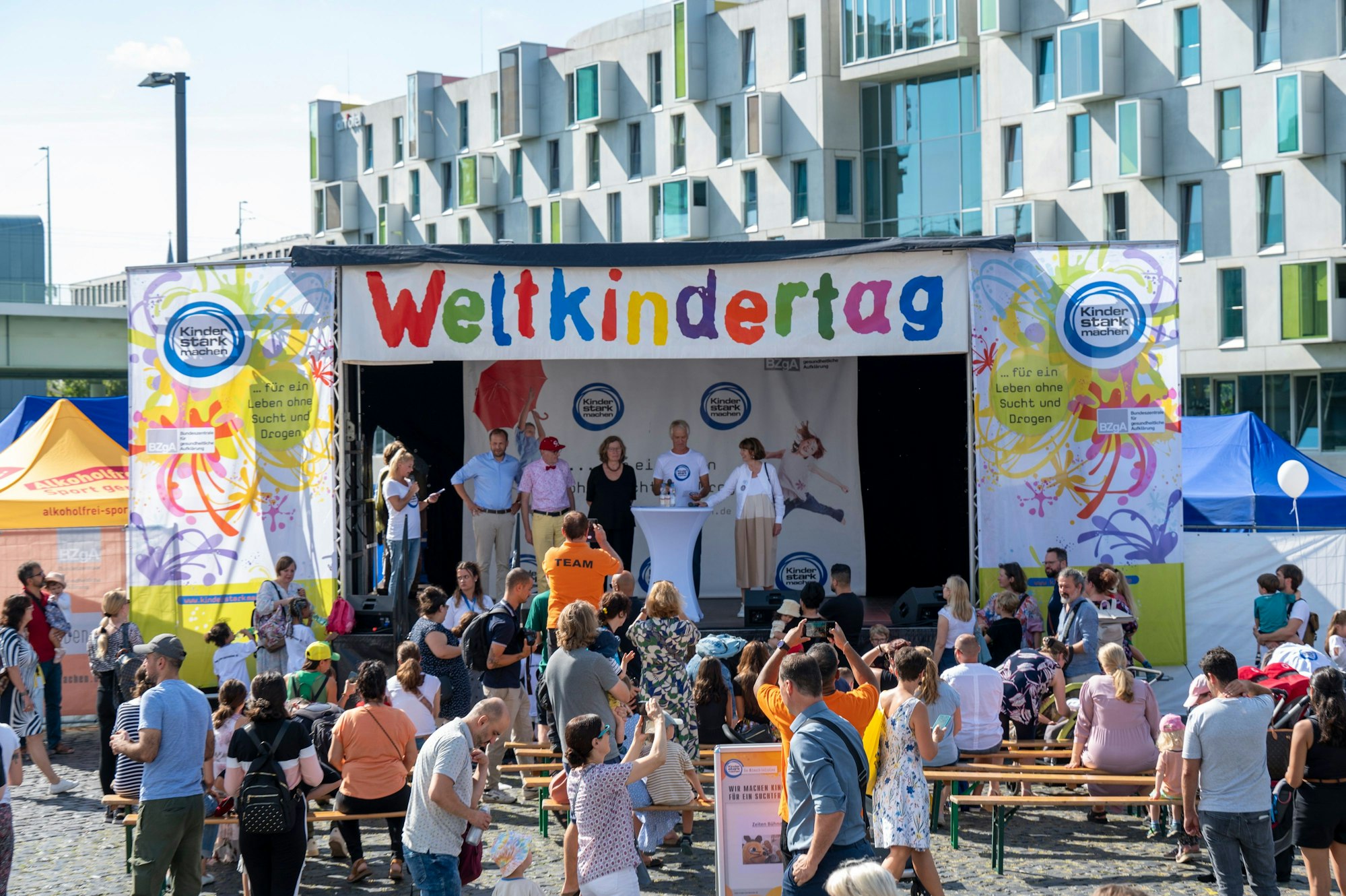 Auf einer großen Bühne im Rheinauhafen eröffnen Vertreterinnen und Vertreter der Stadt und der Organisatoren den Weltkindertag Köln 2024.