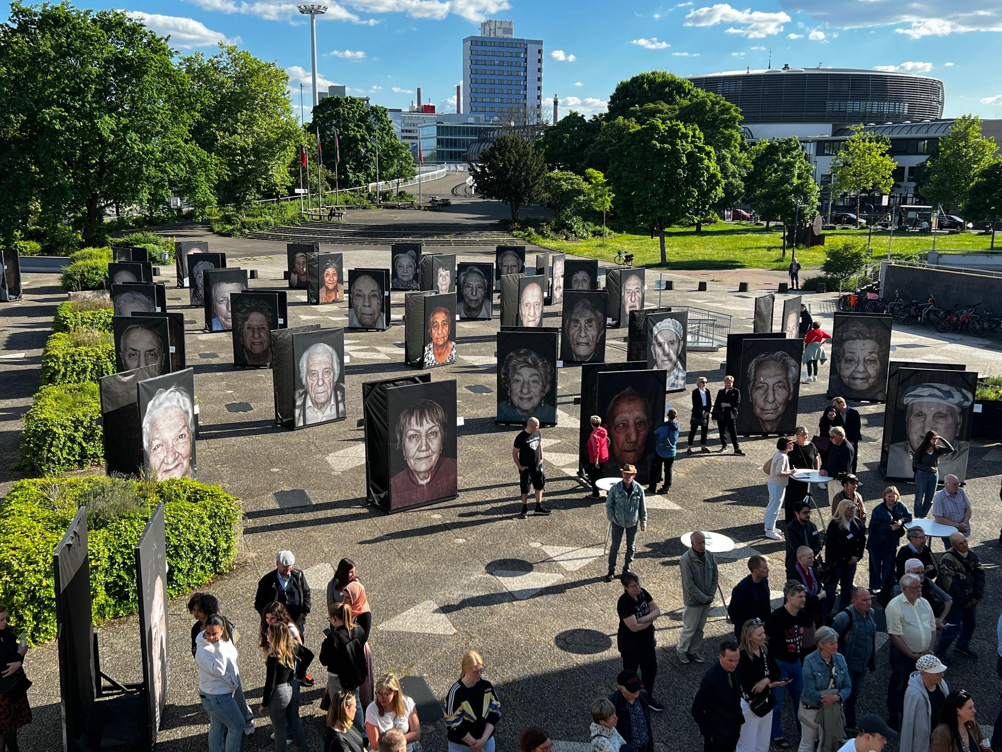 Menschen stehen auf Vorplatz des Forums Leverkusen zwischen großformatigen Fotos.