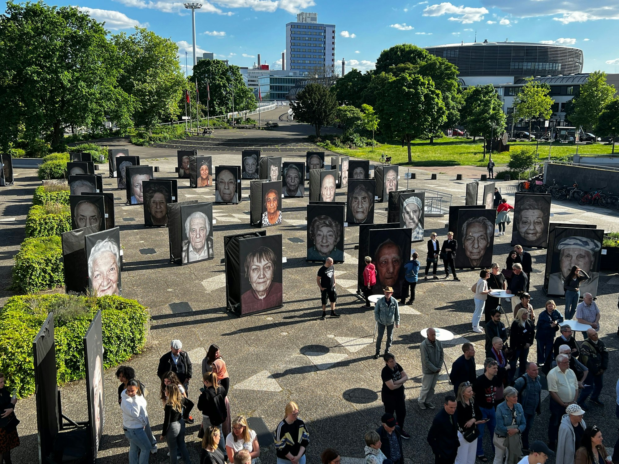 Menschen stehen auf Vorplatz des Forums Leverkusen zwischen großformatigen Fotos.