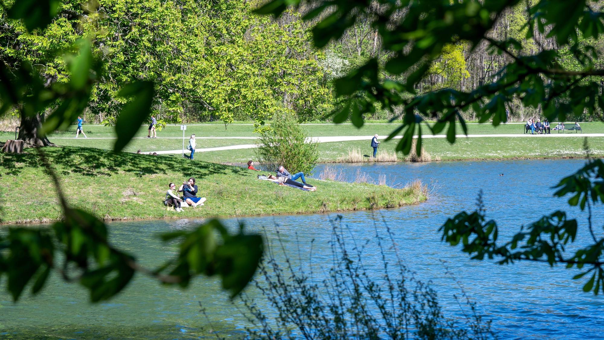 Der Decksteiner Weiher ist ein beliebtes Ausflugsziel. Menschen sitzen auf der Wiese, auf Bänken oder spazieren durch den Park.