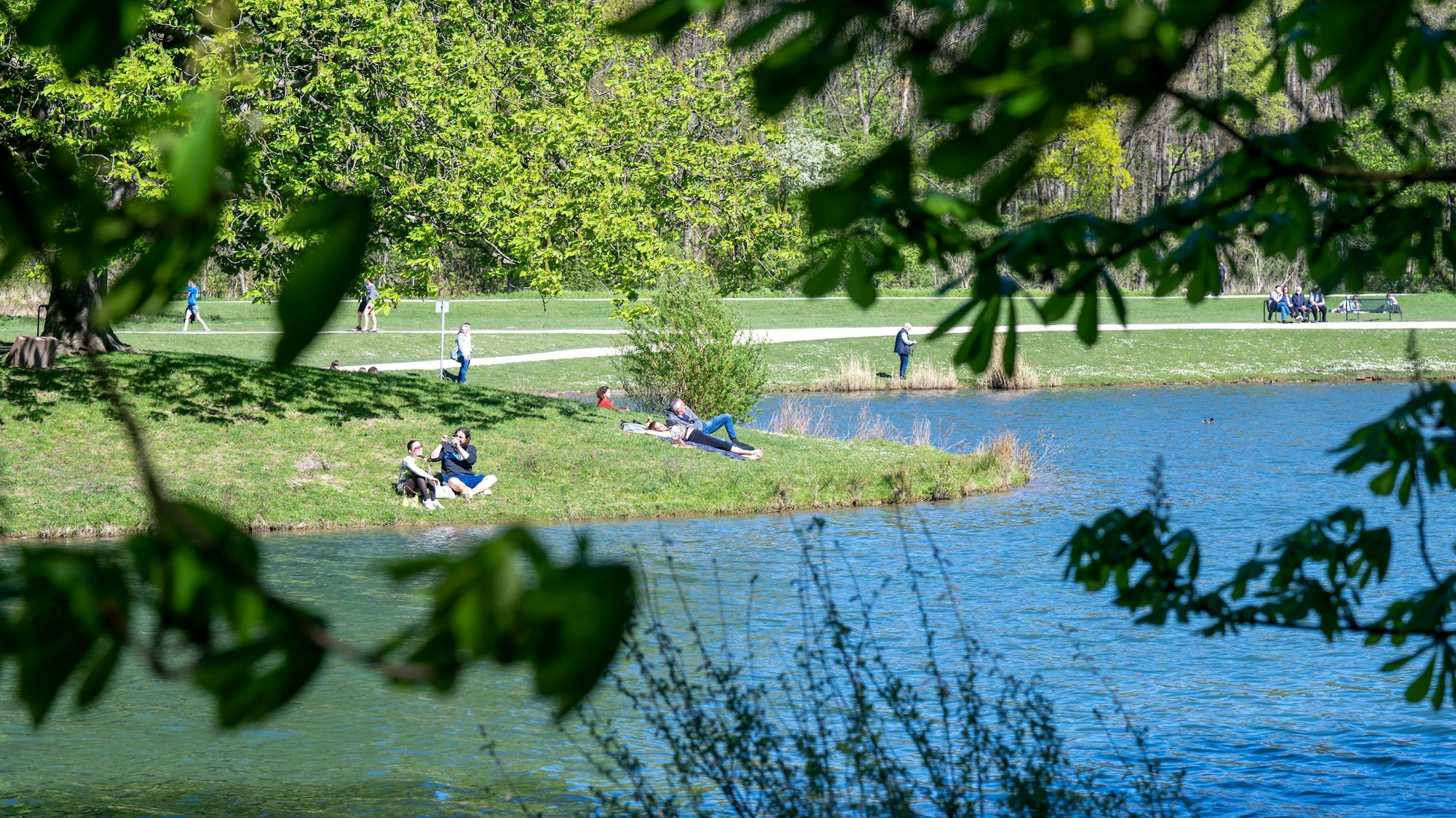 Der Decksteiner Weiher ist ein beliebtes Ausflugsziel. Menschen sitzen auf der Wiese, auf Bänken oder spazieren durch den Park.