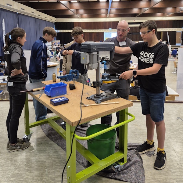 Ein Mann erklärt einem Jugendlichen eine Bohrvorrichtung.