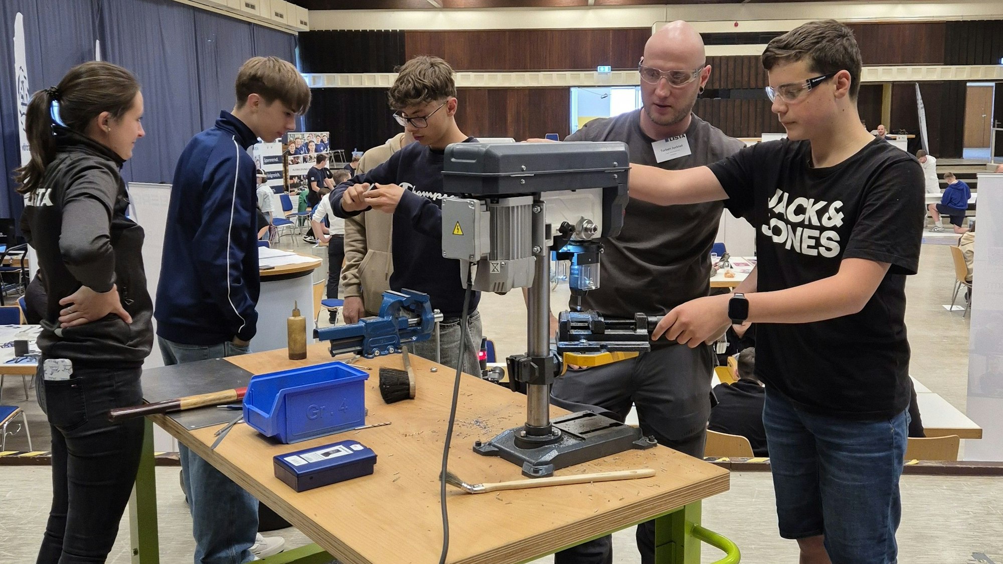 Ein Mann erklärt einem Jugendlichen eine Bohrvorrichtung.