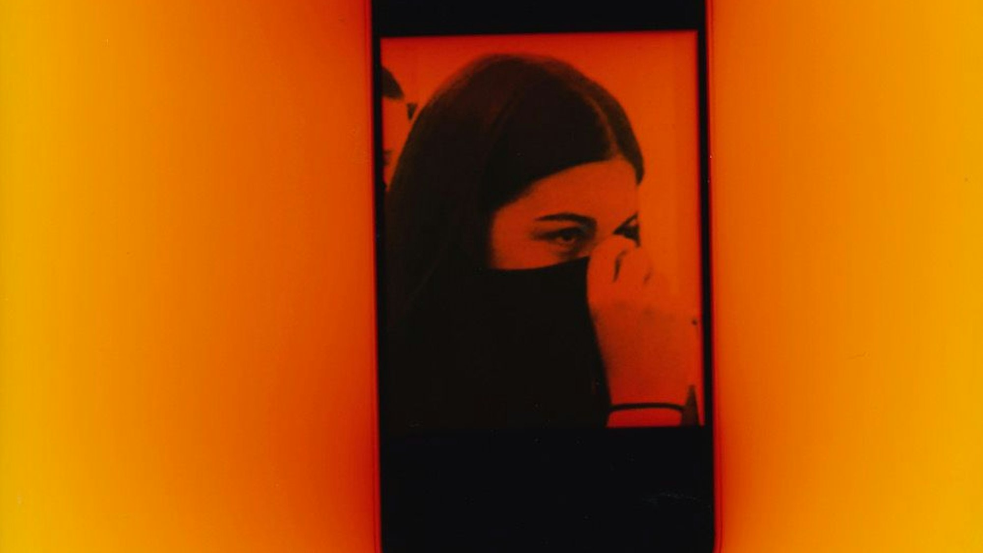 Auf einem Smartphone-Bild verdeckt eine Frau ihr Gesicht.