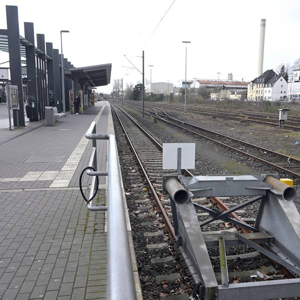 Ein Bahnhof. Der Bahnsteig ist menschenleer, im Vordergrund Bahngleise mit Endpollern.
