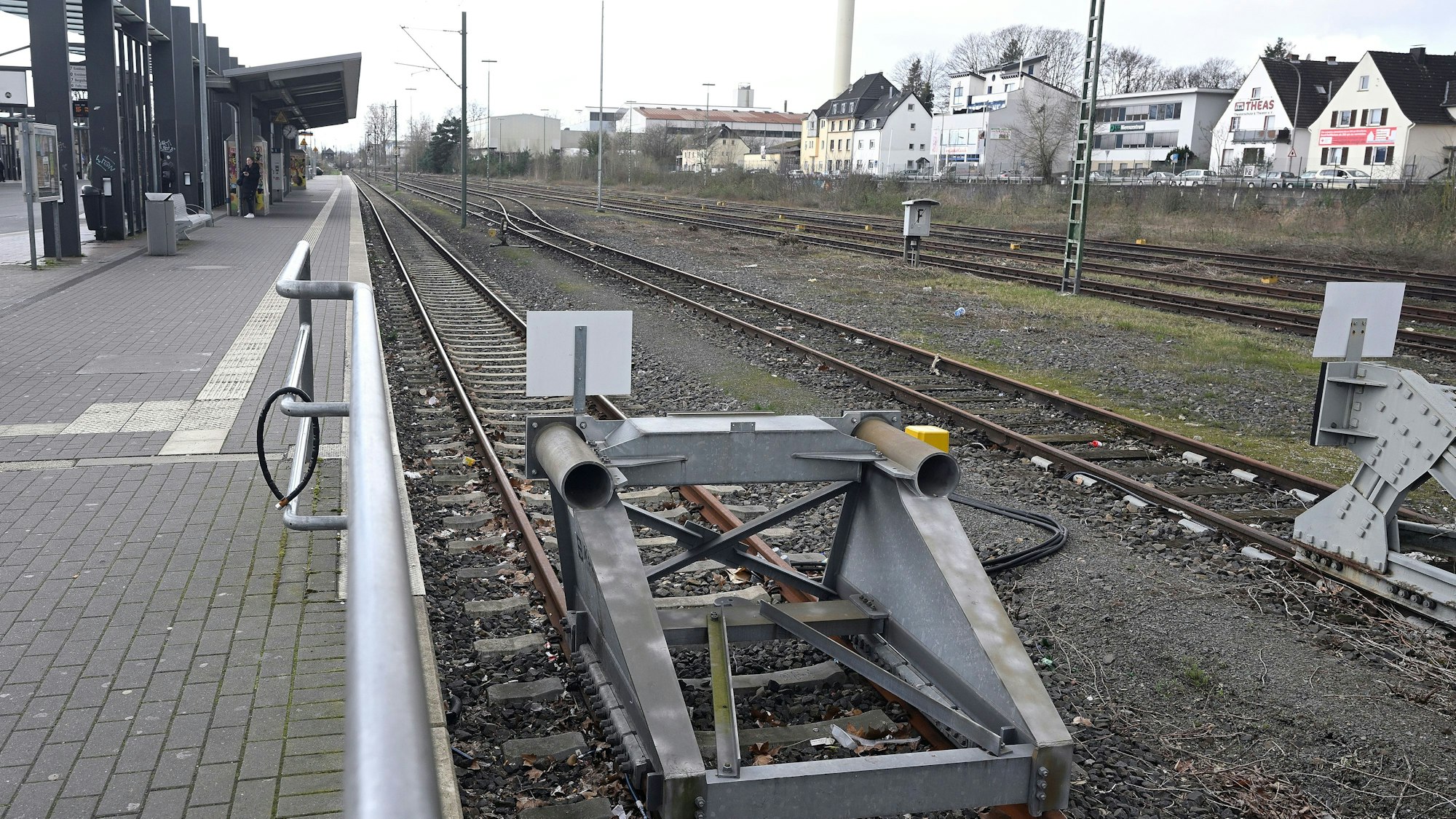 Ein Bahnhof. Der Bahnsteig ist menschenleer, im Vordergrund Bahngleise mit Endpollern.