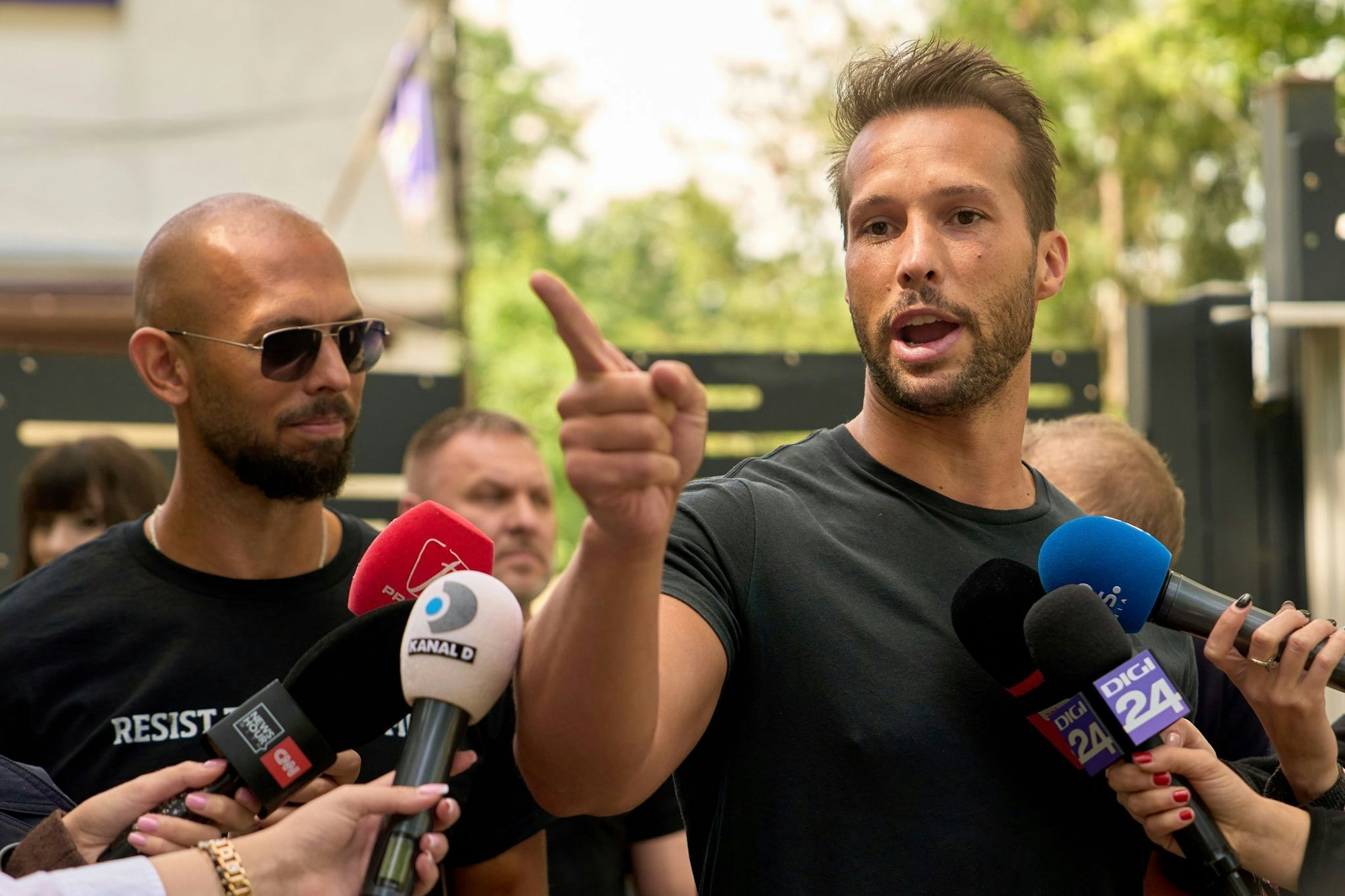 Andrew Tate (links) schaut zu seinem Bruder Tristan Tate, der am 21. Mai vor einer Polizeistation in Voluntari in Rumänien redete.