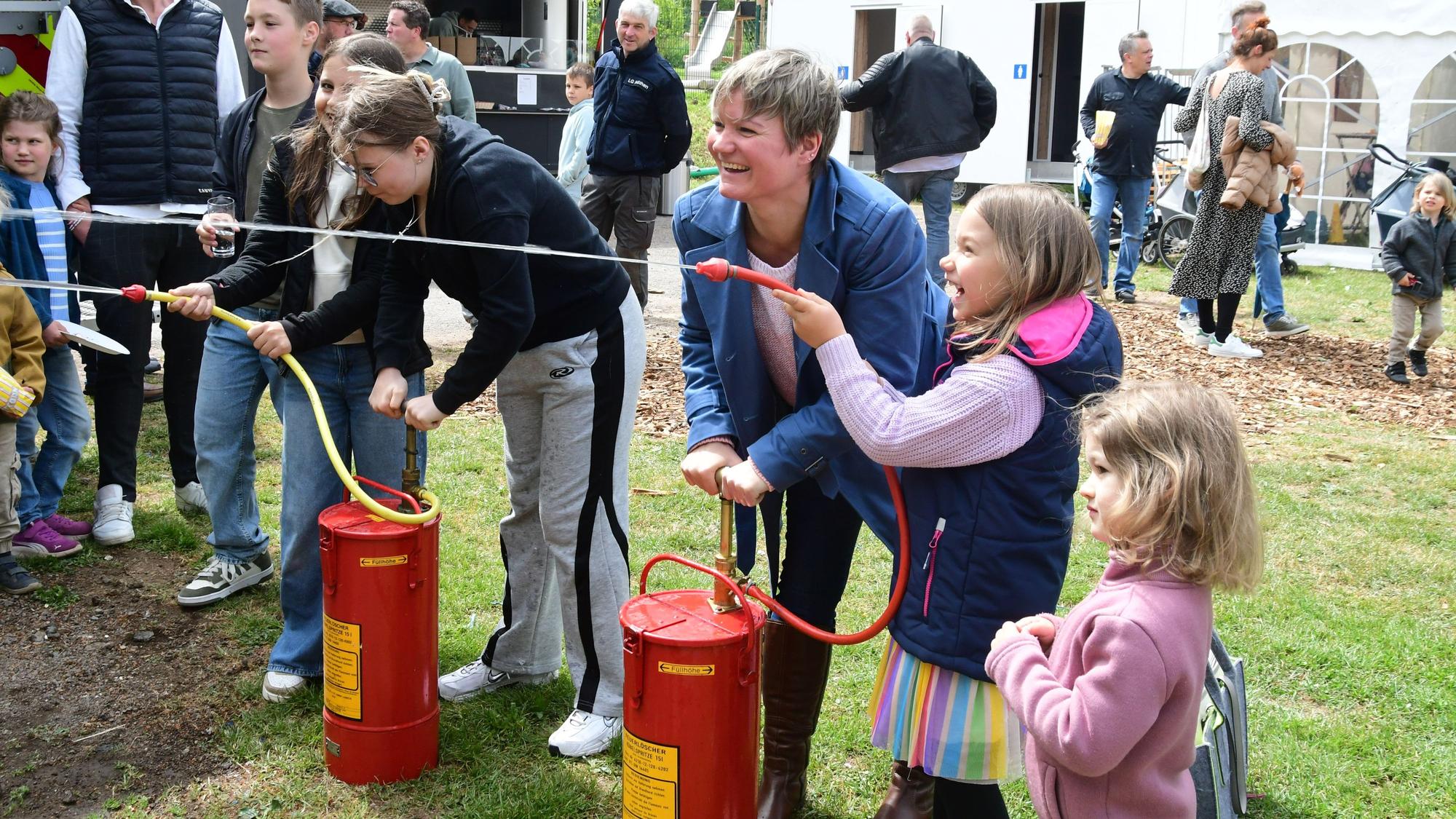 Kinder und Erwachsene stehen an Wasserspritzen und freuen sich, dass sie sie betätigen.