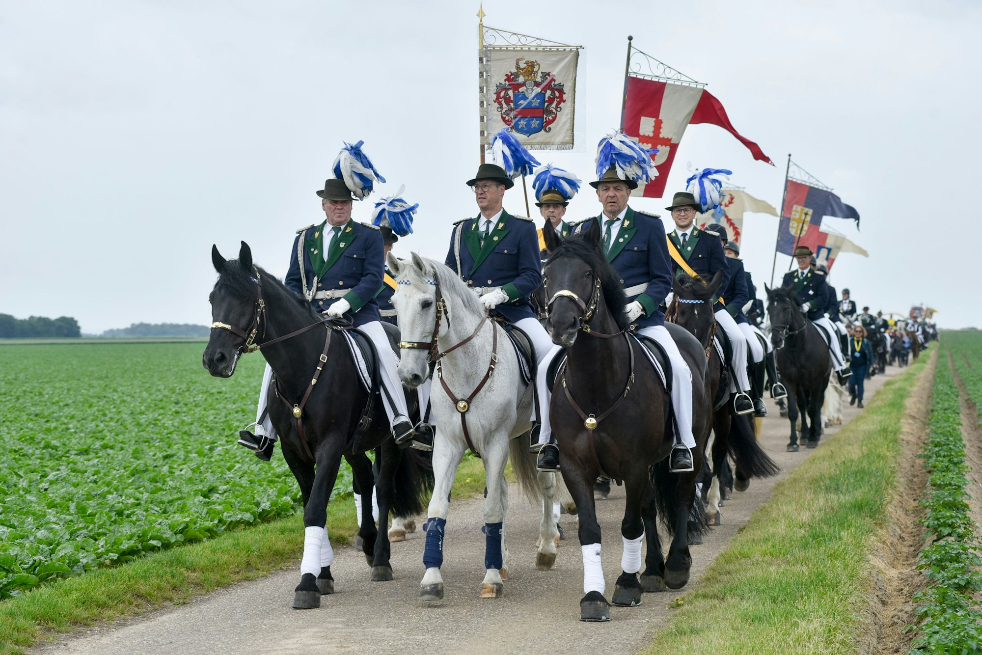 Menschen in Uniformen reiten auf Pferden über einen Feldweg.