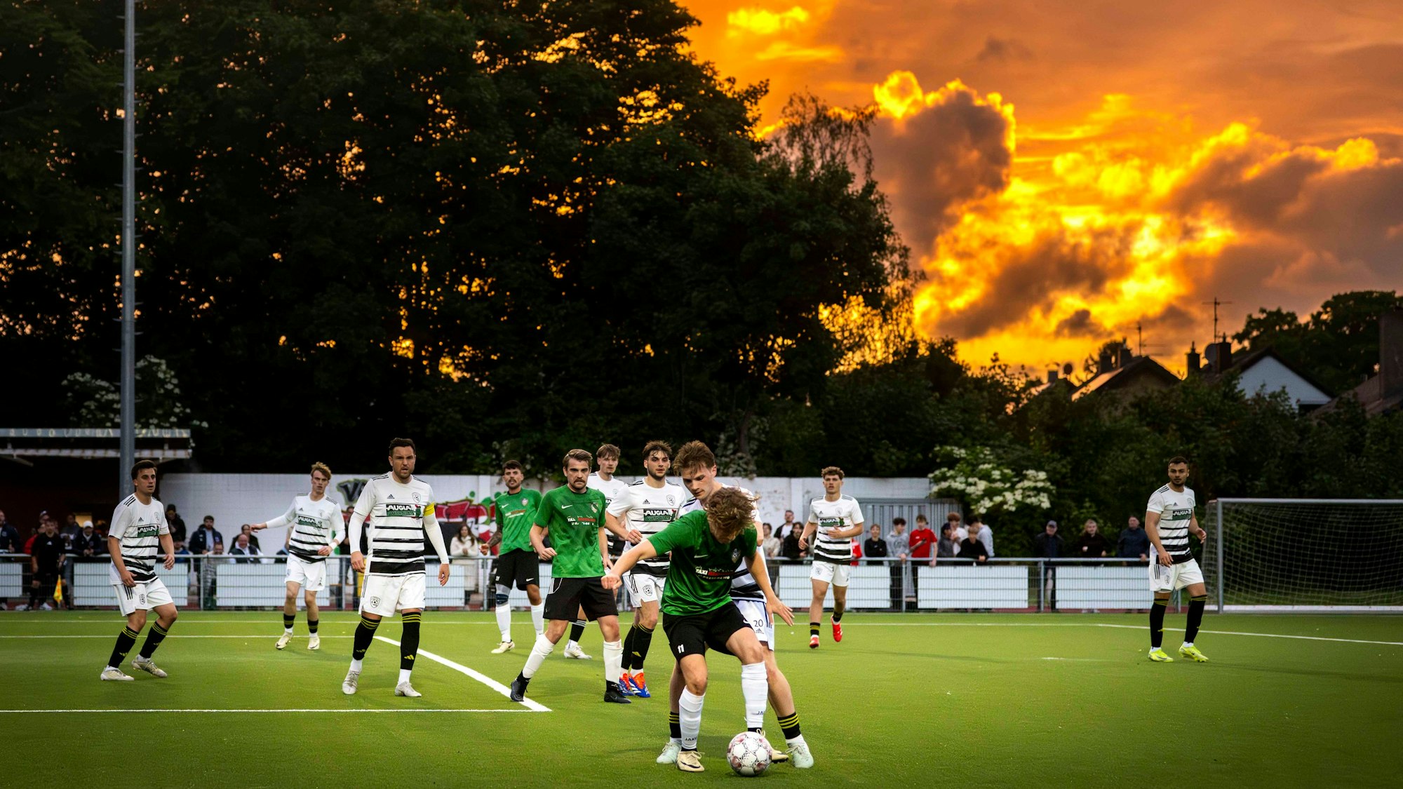 Das Bild zeigt eine Szene eines Fußballspiels. Im Hintergrund geht die Sonne unter.