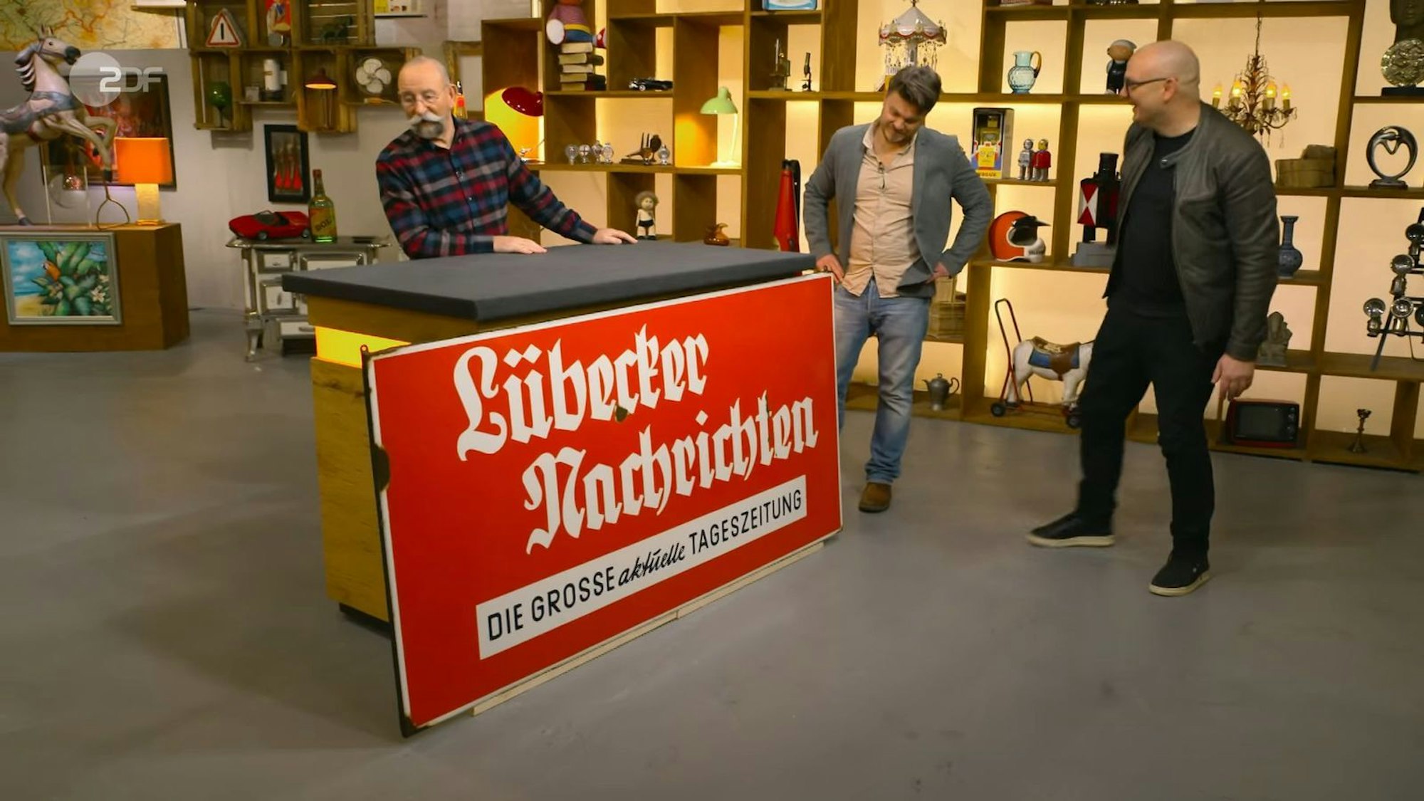 Das zwei Meter breite Emaille-Schild der Lübecker Nachrichten aus den 1950er-Jahren schätzte Sven Deutschmanek auf 500 bis 600 Euro. Christian Vechtel zahlte 1.100 Euro. (Bild: ZDF)