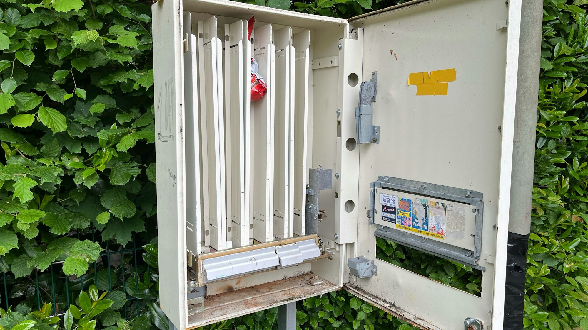 Ein aufgebrochener Kondomautomat steht vor einer Hecke in Odenthal.