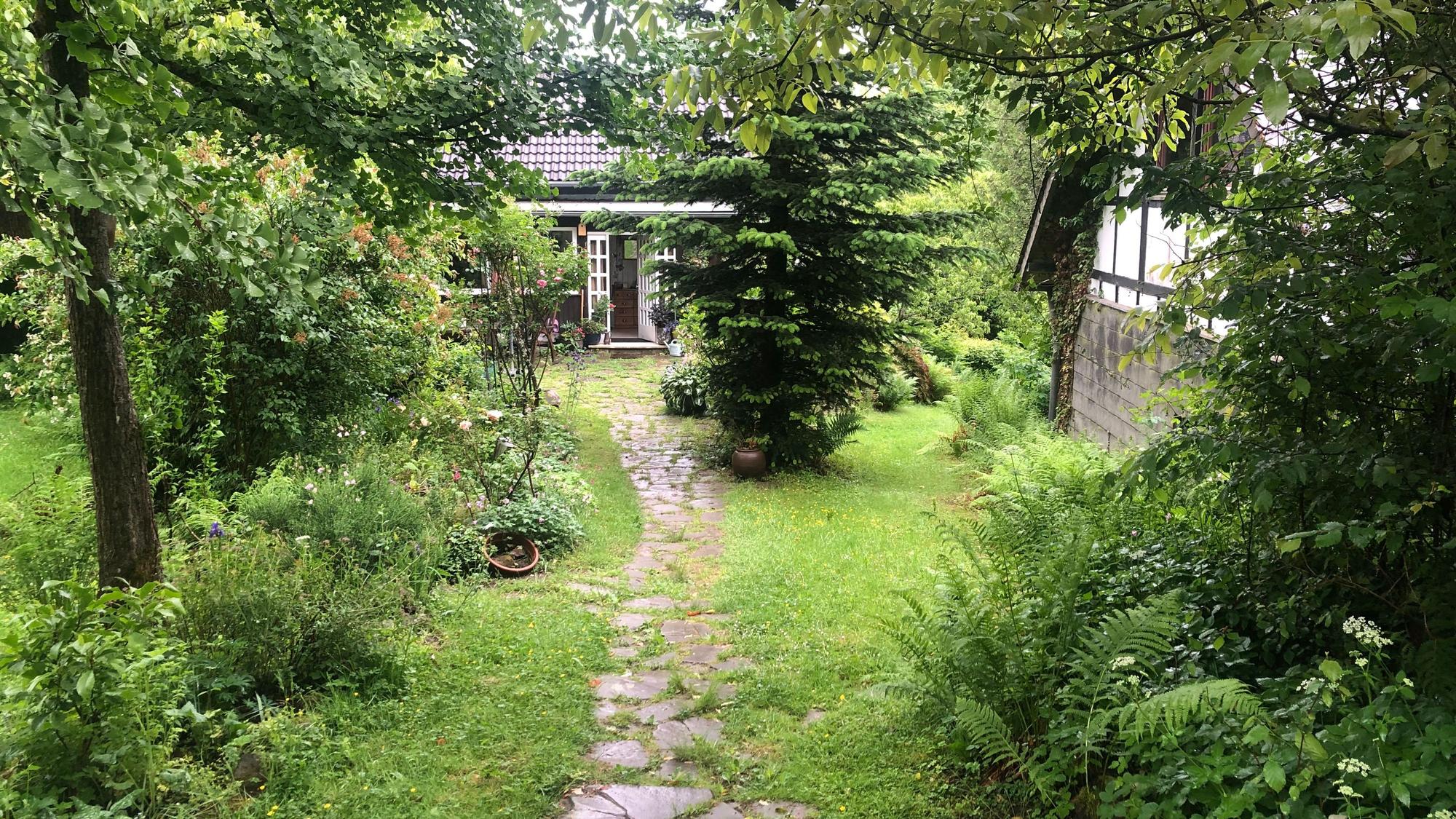 Ein kleines Haus steht am Ende eines kleinen Weges, der durch einen idyllischen Garten führt.