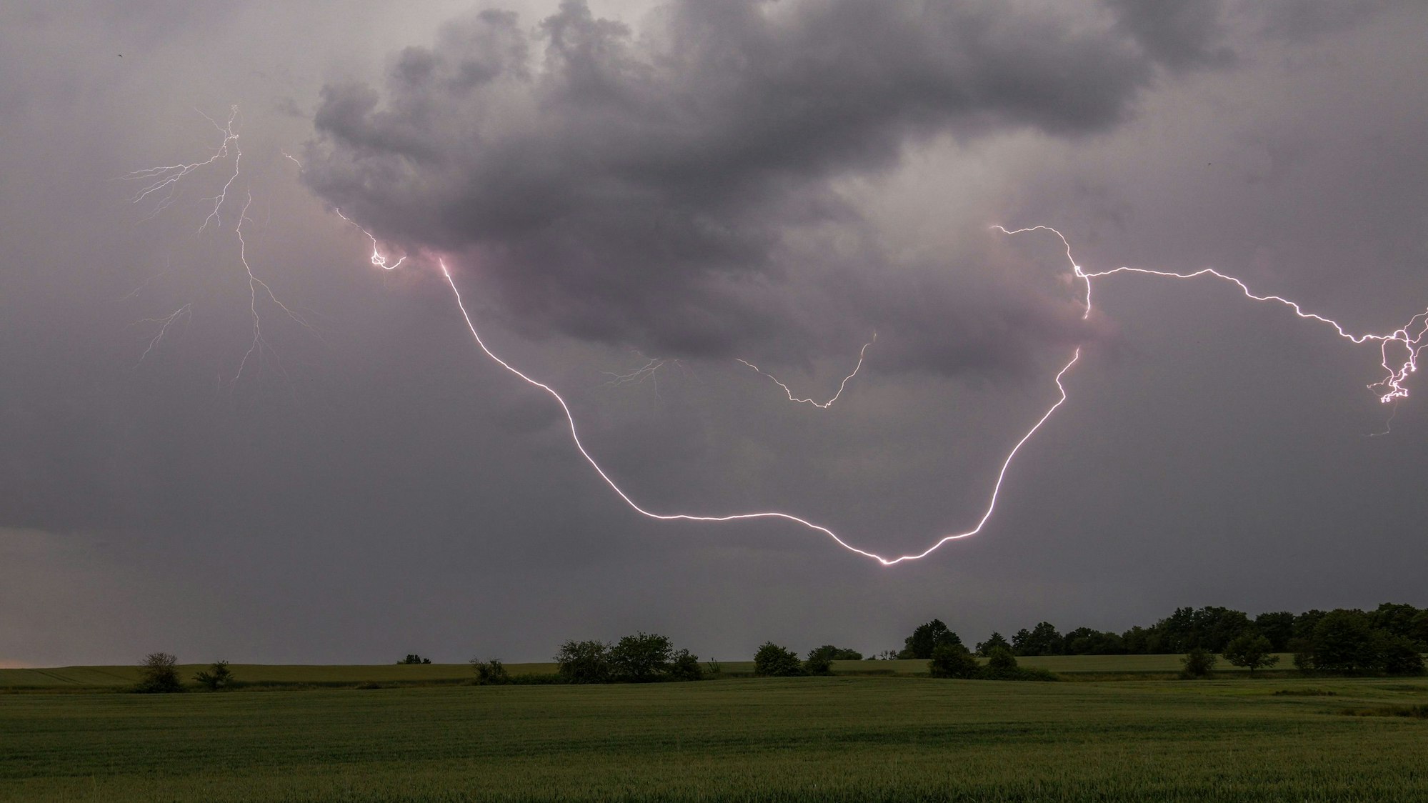 Blitze eines Gewitters erhellen die dunklen Wolken über der Landschaft. In NRW toben am Wochenende schwere Gewitter, warnt der Deutsche Wetterdienst. (Symbolbild)