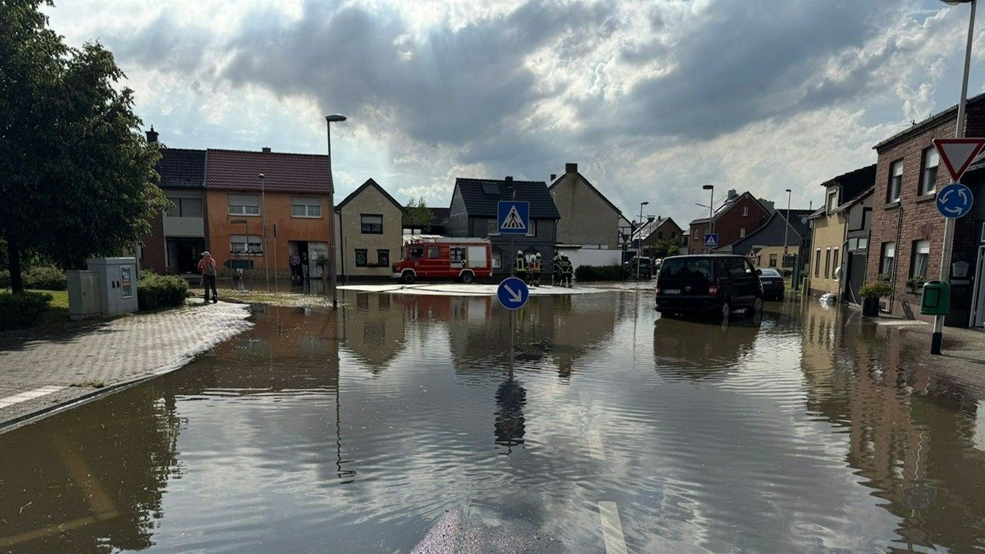 Das Bild zeigt eine überflutete Straße, im Hintergrund Häuser.