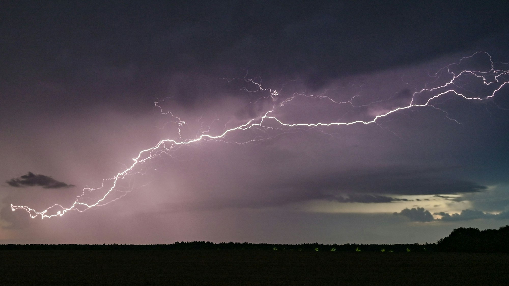 Blitze eines Gewitters erhellen die dunklen Wolken über der Landschaft.