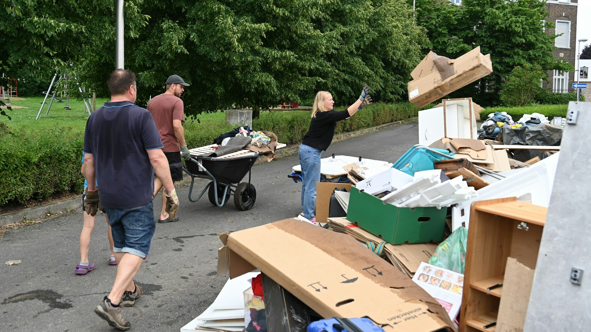 Bewohner werfen durchnässte Kartons auf einen Haufen Sperrmüll. Andere transportieren zerstörte Habseligkeiten mit Schubkarren.