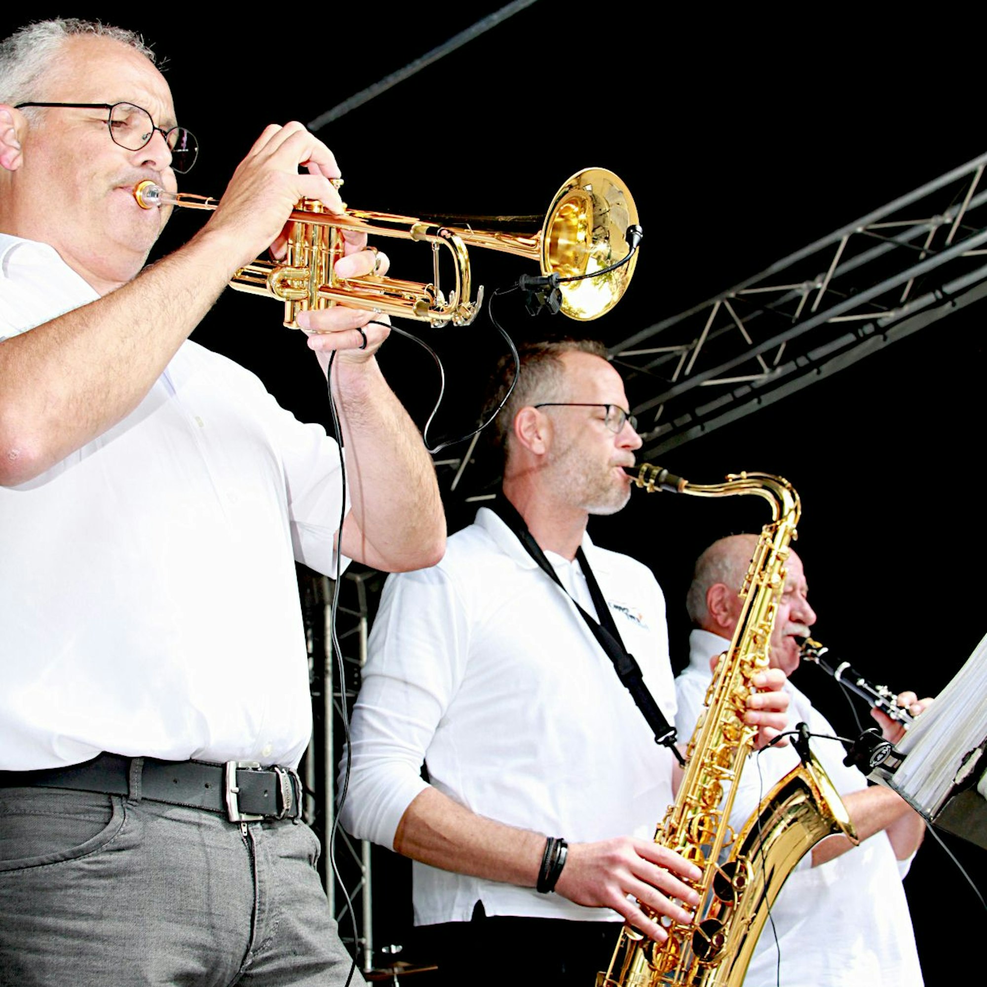 Drei Musiker mit Trompete, Saxophon und Klarinette auf der Bühne.