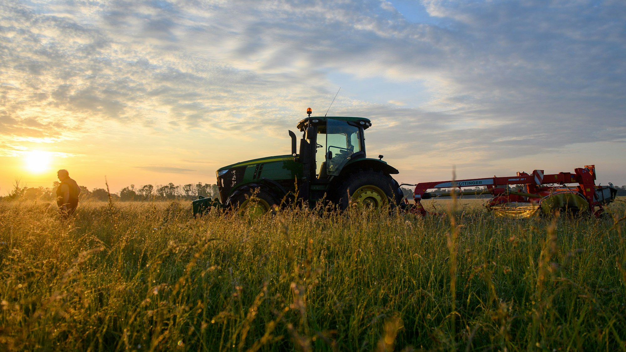 Ein Traktor steht vor der aufgehenden Sonne auf einem Feld.