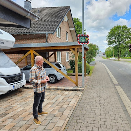 Peter Przybecki steht in seiner Einfahrt und schaut auf die Geschwindigkeitsanzeige. Ein Lkw fährt vorbei.