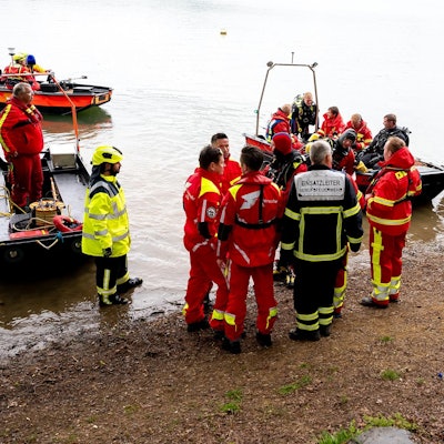 Uniformierte Männer mit Booten am Ufer der Talsperre.