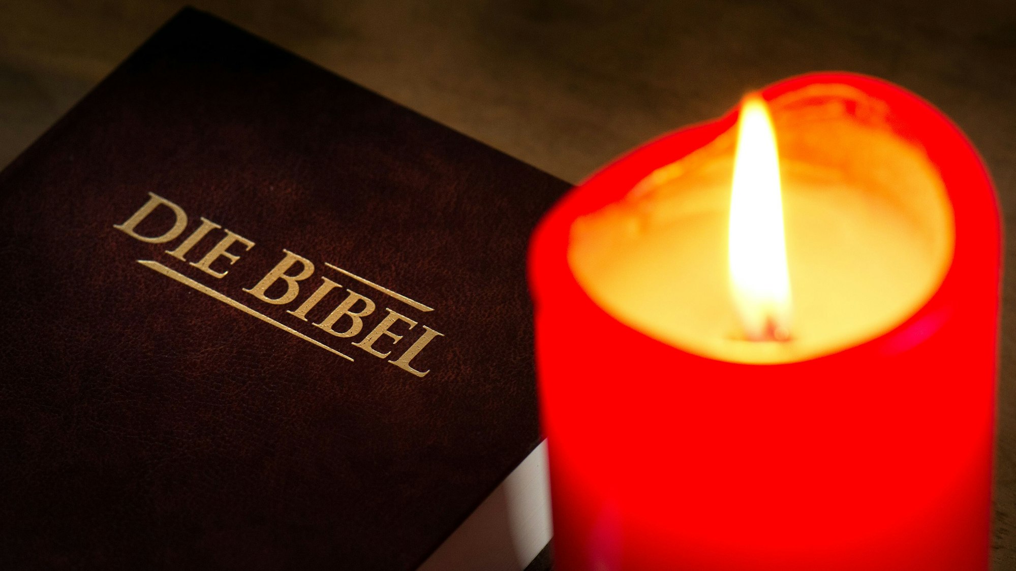 Eine brennende rote Kerze steht neben einer zugeklappten Bibel