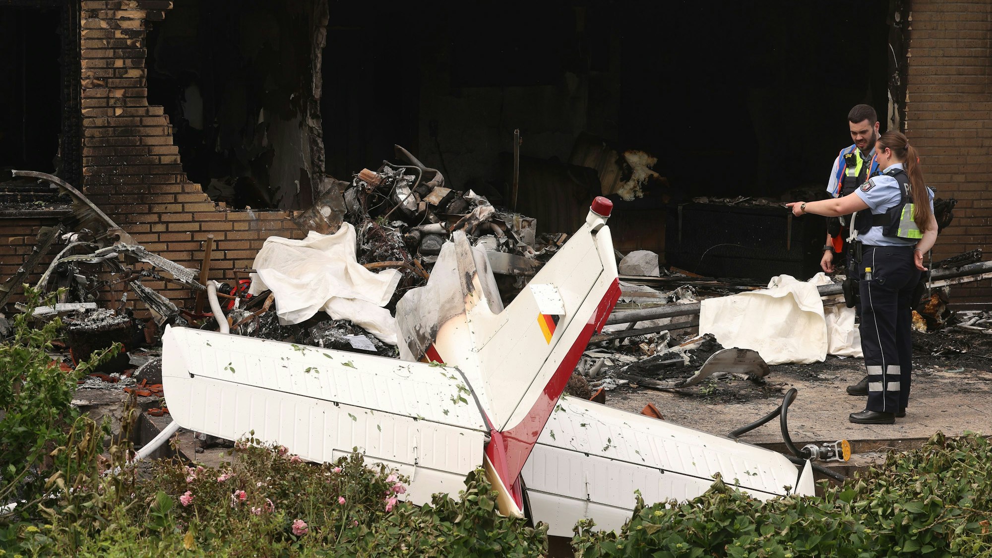 Polizisten schauen sich auf der Terrasse eines Wohnhauses die Reste eines abgestürzten Flugzeugs an.