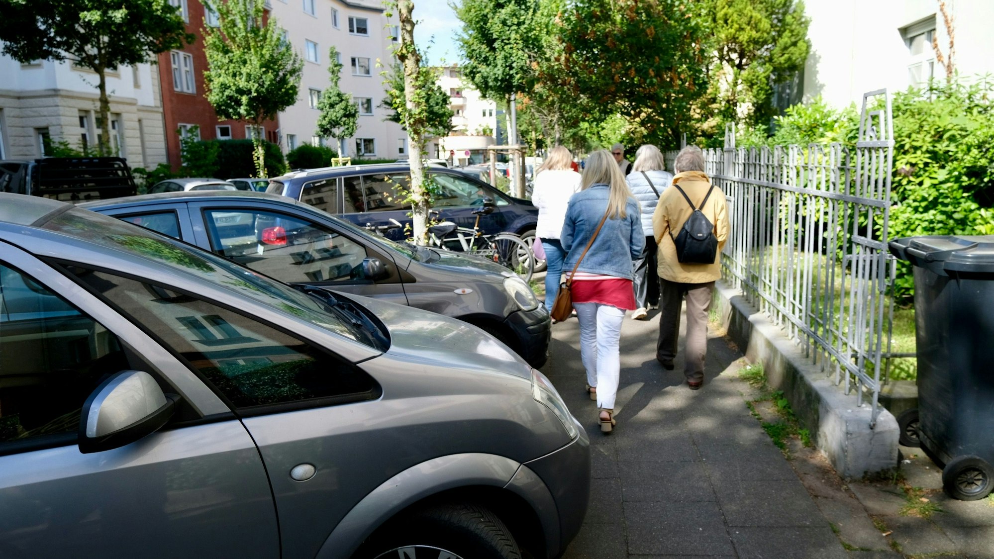 Vier Frauen laufen auf einem Bürgersteig an parkenden Autos vorbei, die einen Teil des Bürgersteigs einnehmen.