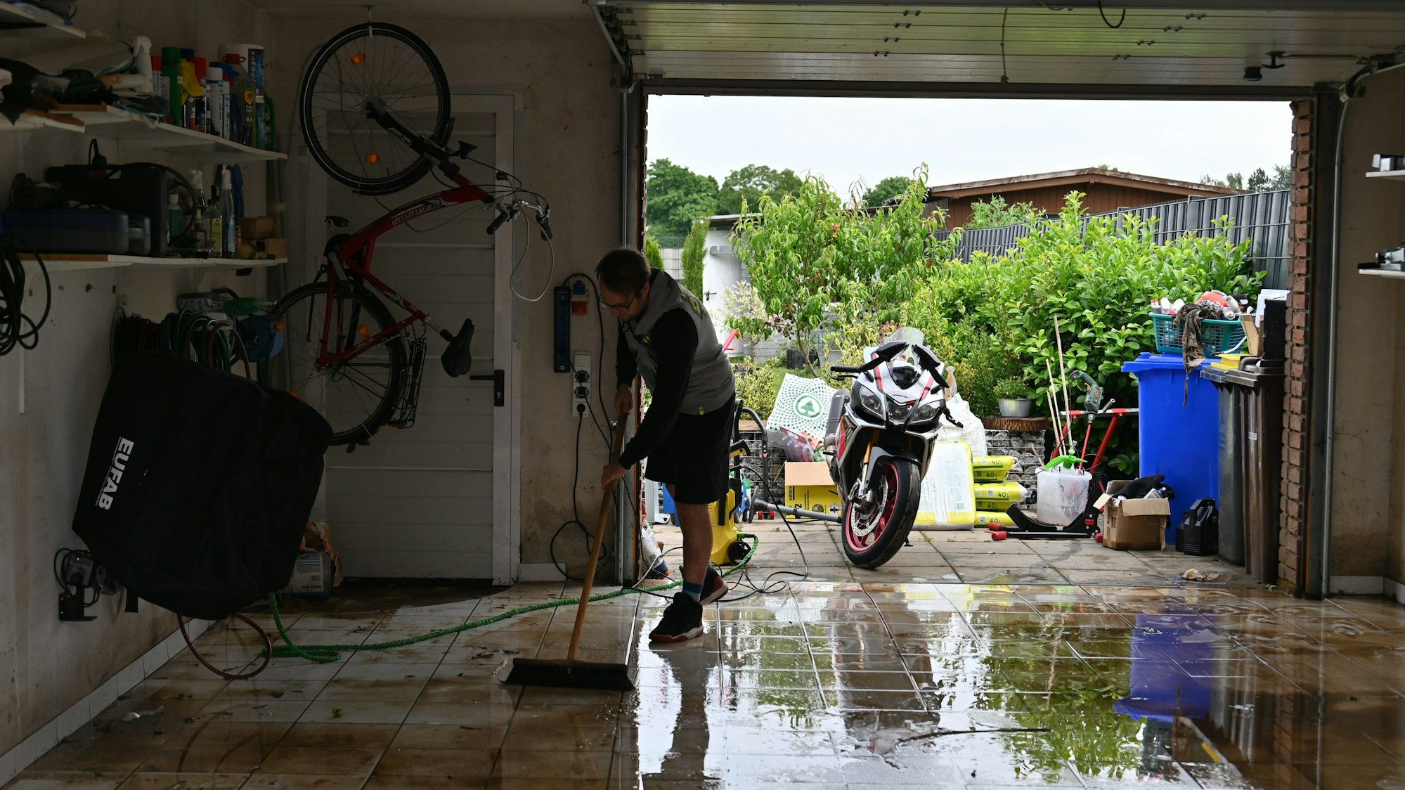 Ein Anwohner wischt mit einem Besen das dreckige Wasser aus seiner Garage.
