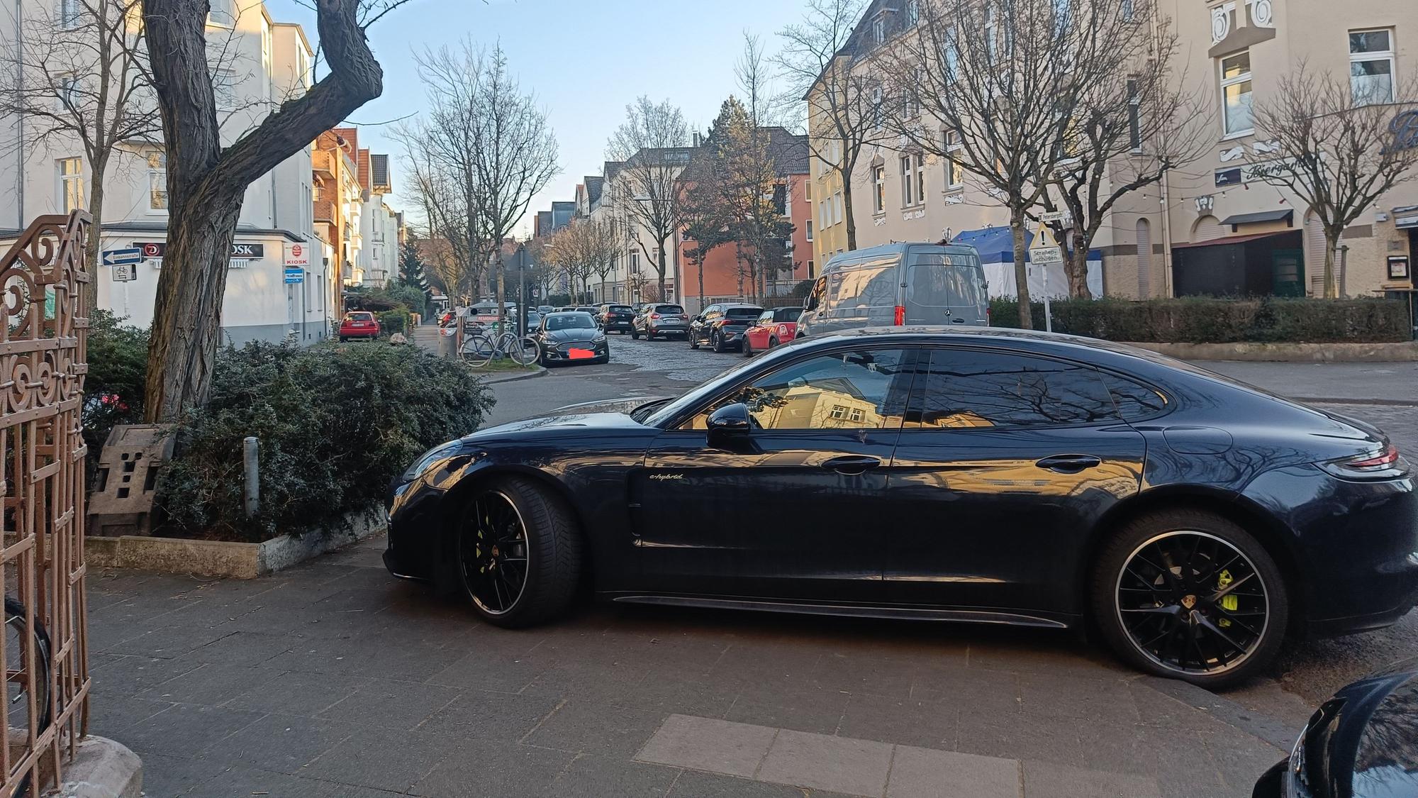 Ein Auto steht auf einem Gehweg, so dass Fußgänger die Straße nicht überqueren können.