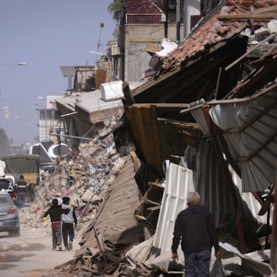 Anwohner gehen auf einer Straße an den Trümmern von Gebäuden vorbei, die durch das Erdbeben vom 6. Februar beschädigt wurden.