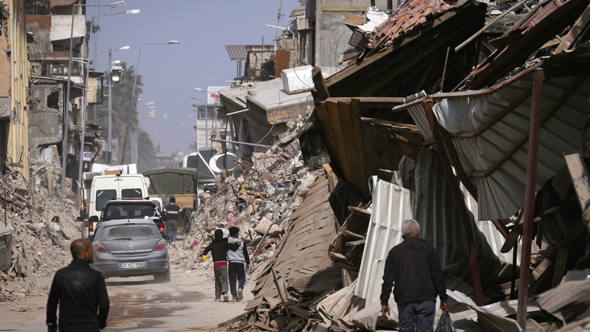 Anwohner gehen auf einer Straße an den Trümmern von Gebäuden vorbei, die durch das Erdbeben vom 6. Februar beschädigt wurden.