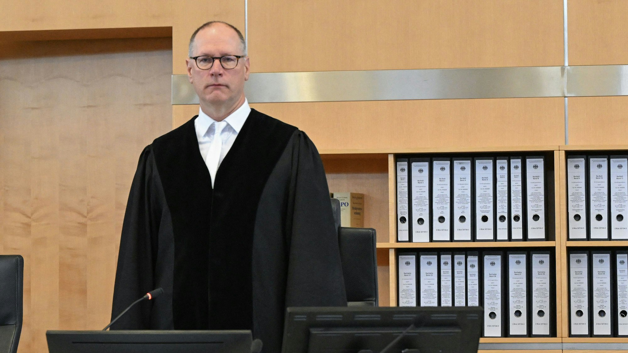 Winfried van der Grinten ist am Gericht in Robe zu sehen. Er steht vor einer Schrankwand mit Ordnern.