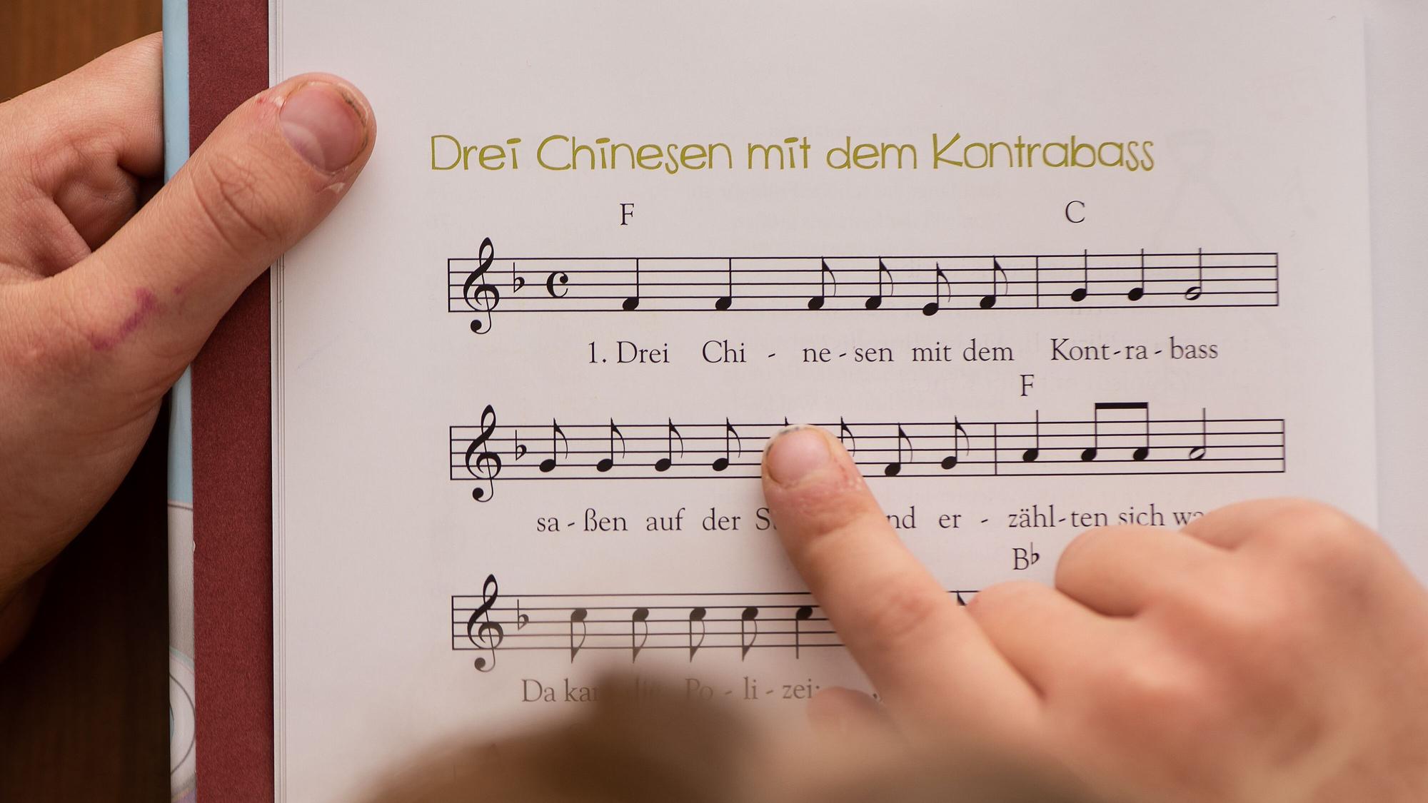 Ein Mädchen hält ein Kinderlieder-Buch in der Hand mit Noten des Liedes "Drei Chinesen mit dem Kontrabass".